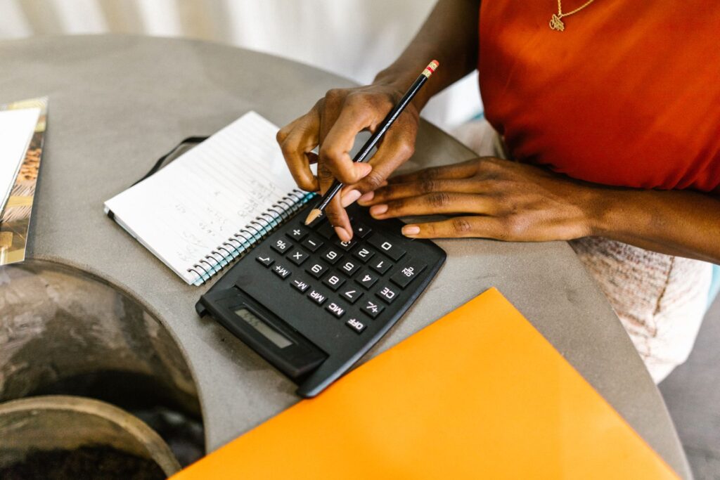 Person using a calculator and notebook to work through financial calculations at a desk, epresenting financial planning and sales forecasting for a startup.